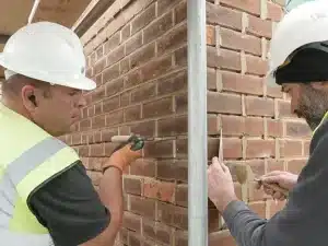 Two construction workers in hard hats and safety vests repointing brickwork, demonstrating professional brick restoration techniques for structural integrity and aesthetic appeal.