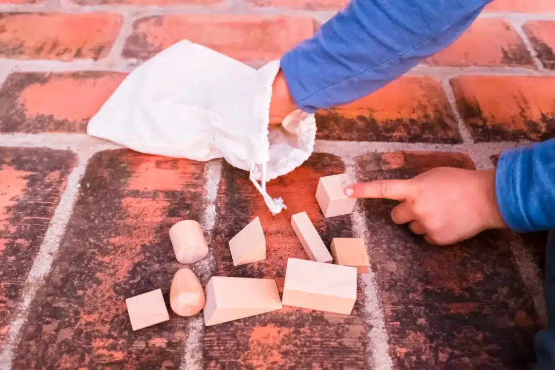Child's hand pointing at wooden building blocks scattered on a brick surface, emphasizing safe play and maintenance of brick surfaces.