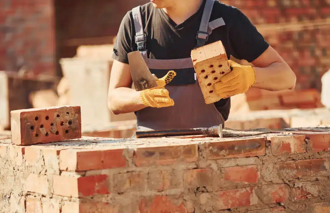 Builder inspecting bricks and preparing for construction, emphasizing brick quality assessment for safety and durability.