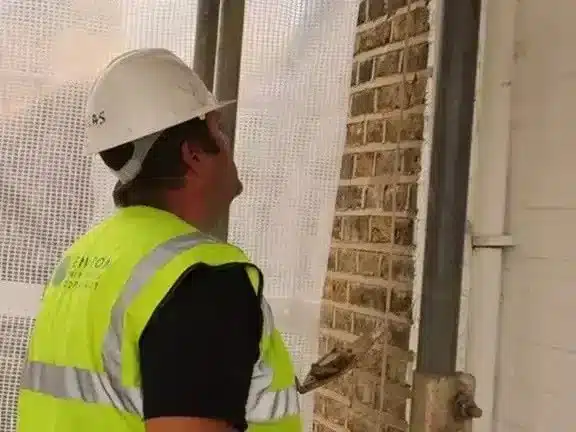 Residential building showing damp damage with a construction worker assessing moisture issues